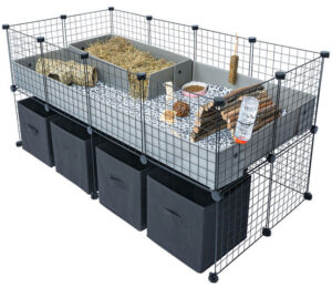 C&C guinea pig cage with a raised correx base, hay tray, food bowls, water bottle, and wooden chew toys, with black storage cubes underneath.
